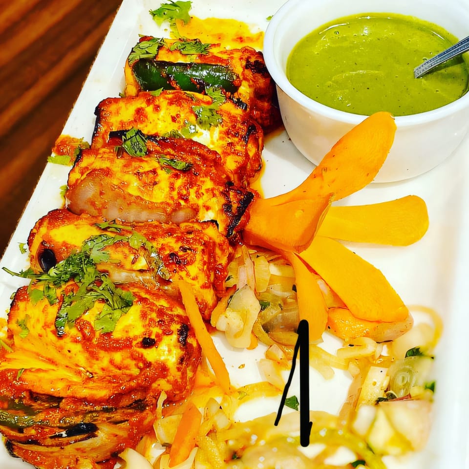 Taj India Restaurant's paneer tikka with green chutney, onions, and carrot garnish.