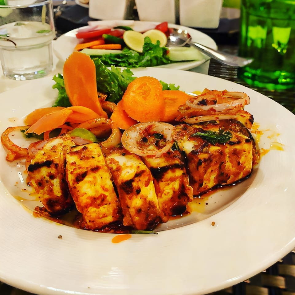Grilled paneer tikka with onions, carrots, and lettuce on a white plate at Taj India Restaurant.