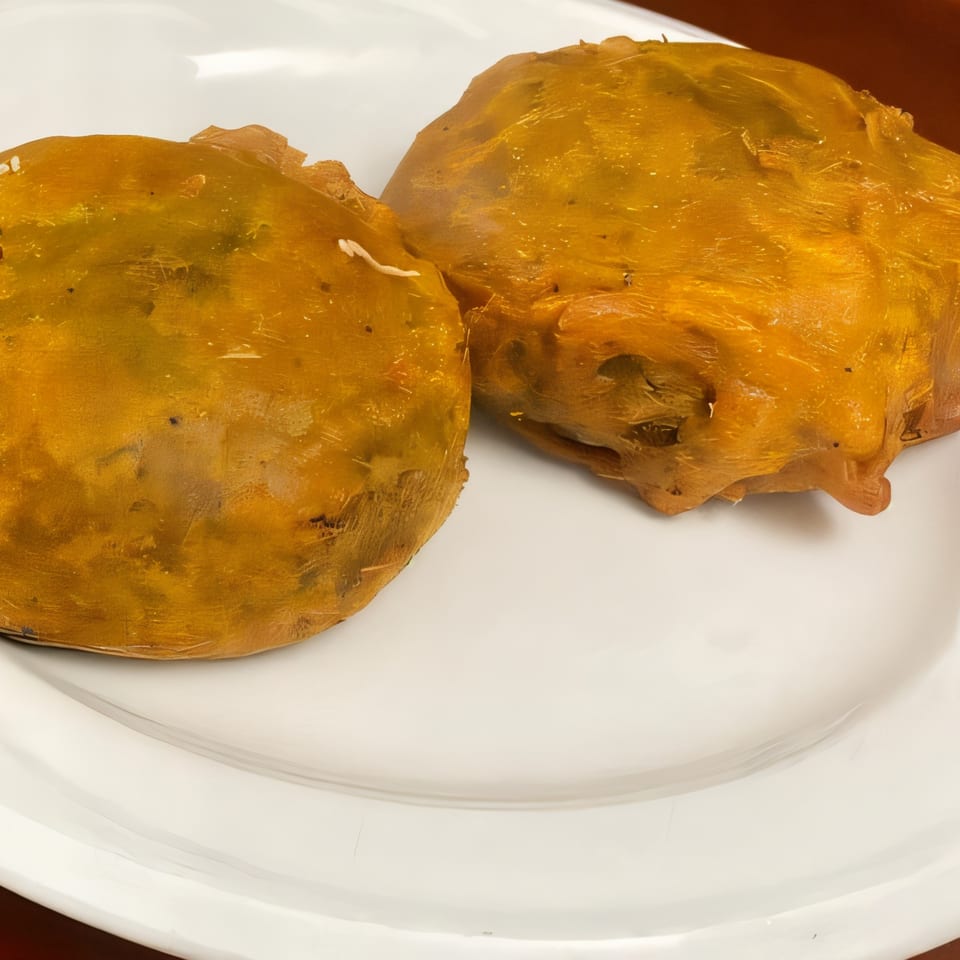 Two golden-brown Indian pastries, possibly samosas, on a white plate.