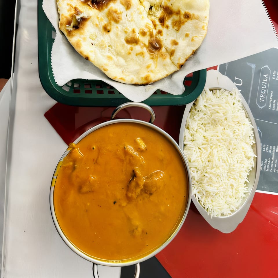 Taj India Restaurant's butter chicken, basmati rice, and naan bread on a red and white table.