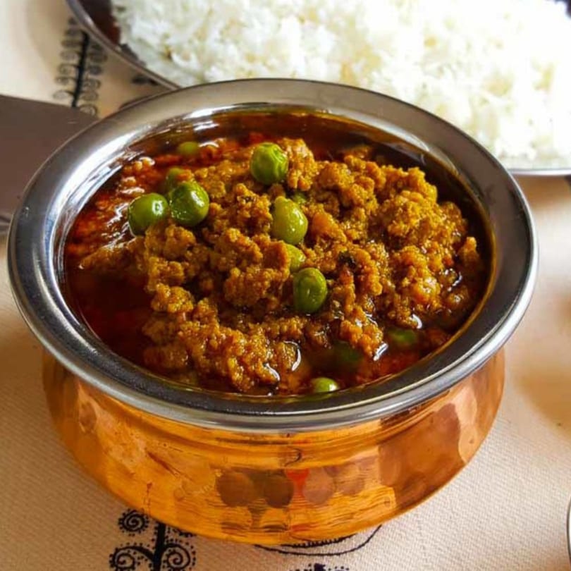 A copper bowl of keema matar, a spiced ground meat and pea dish, with white rice in the background.