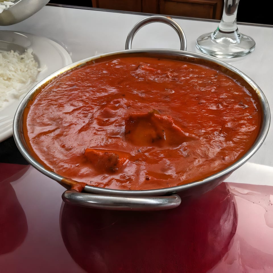 A metal karahi bowl filled with rich, red Indian curry, with a side of white rice.